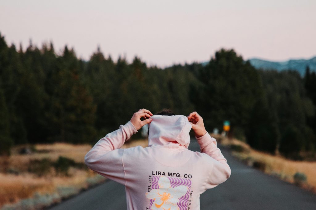Person in a hoodie on a road surrounded by pine trees in Truckee, CA.