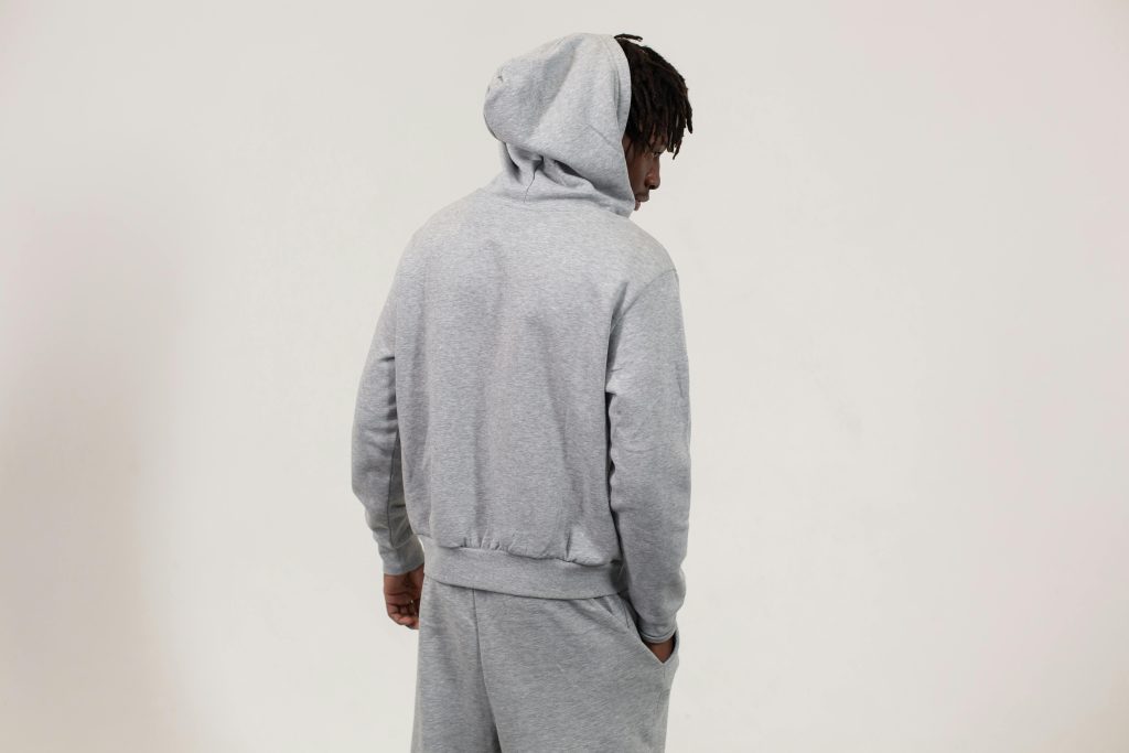 Back view of an adult male in a gray hoodie posing in a studio setting.